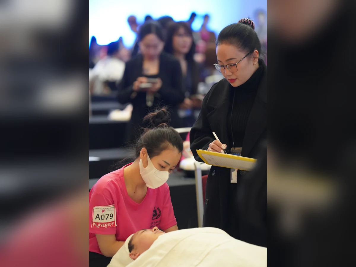 Thí sinh áo hồng thực hành chăm sóc da, bên cạnh có người quan sát và ghi chép.